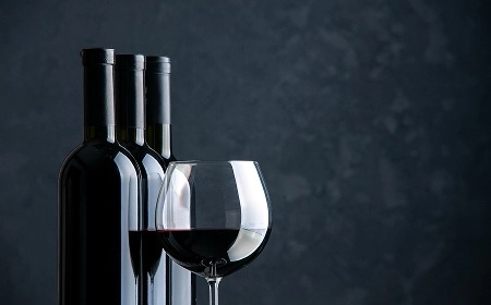 Три бутылки красного вина и бокал с вином на тёмном фоне